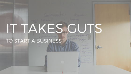 THE TEXT "IT TAKES GUTS TO START A BUSINESS" OVER PHOTO OF MAN IN MID-20S TYPING ON SILVER LAPTOP IN FRONT OF A WHITEBOARD WITH WRITING ON IT