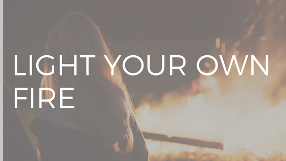 WHITE TEXT READING "LIGHT YOUR OWN FIRE" OVER PHOTO OF WOMAN WITH LONG BLONDE HAIR LOOKING AT A BLAZING BONFIRE