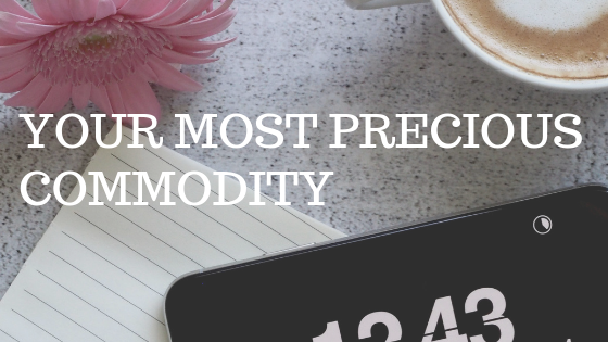 Flatlay image of a tabletop with a flower, cup of coffee, and a mobile phone with a clock setting. White text reading "your most precious commodity"