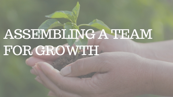 TWO HANDS holding a green plant with the white text "assembling a team for growth"
